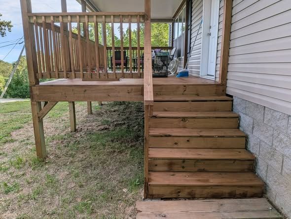 Rebuilt deck stairs and railing beside a vinyl-sided house