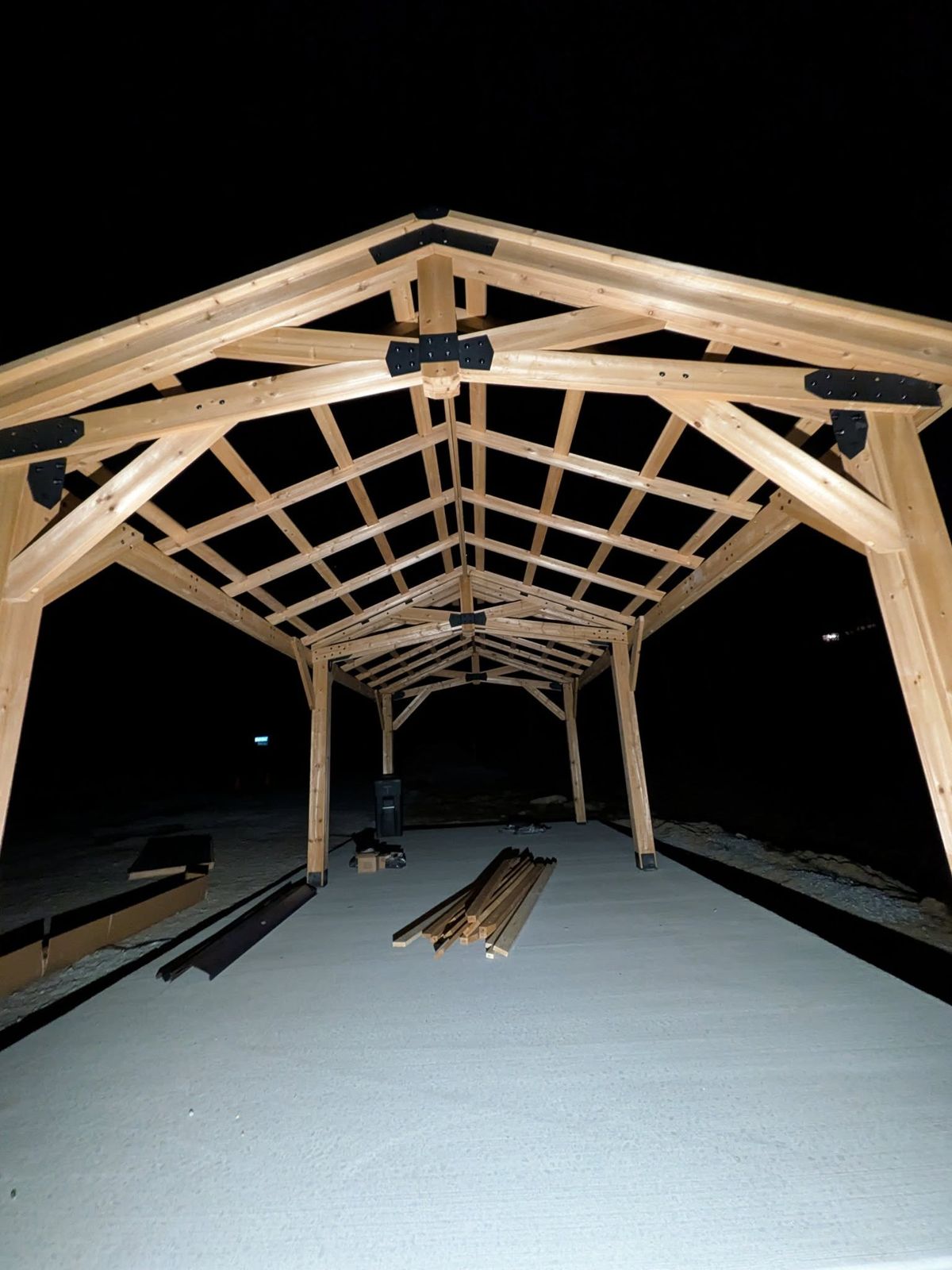 Timber pavilion trusses lit up at night during the build